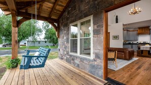 A wooden porch with a swing, a stone wall, and a view into a modern kitchen.