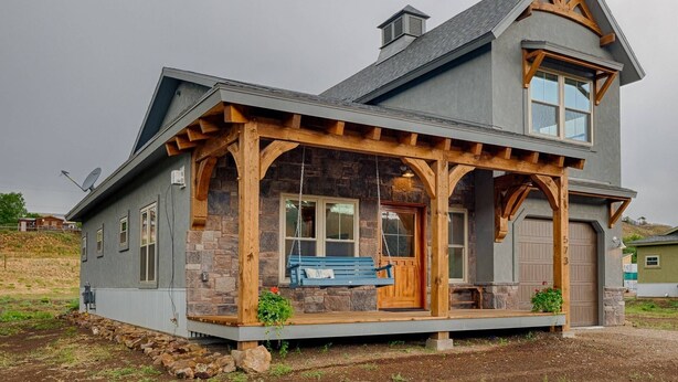 A two-story house with a stone facade, a wooden porch with a swing, and a garage.