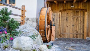 Une porte en bois rustique, ornée d’une grande roue en bois, un mur de pierres et un chemin de gravier menant à la porte.