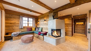 L’intérieur d’un chalet confortable, avec une cheminée en pierre, des poutres en bois et un coin salon agrémenté de coussins.