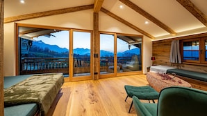 Une pièce spacieuse avec des poutres en bois, une grande porte-fenêtre coulissante donnant sur un balcon avec vue sur les montagnes, un lit et un coin salon avec vue.