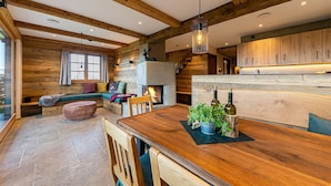 Un intérieur chaleureux de style chalet, avec des poutres apparentes, une cheminée, un coin repas et une cuisine dotée de meubles en bois.