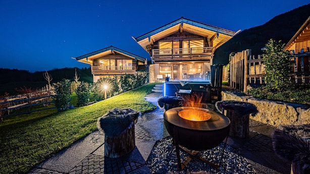 Un chalet en bois à deux étages, doté d’un foyer extérieur et d’un espace salon extérieur.