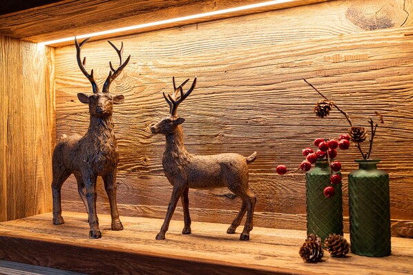 A wooden wall with two deer sculptures and two green vases with red berries and pinecones.