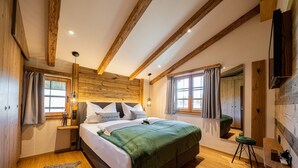 Un dormitorio con una cama grande, vigas de madera, una colcha verde y una decoración de estilo rústico.