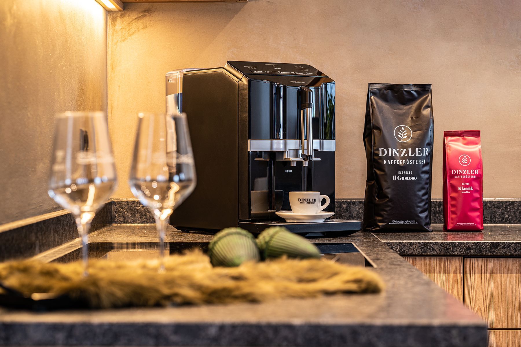 Une machine à café, deux verres, une tasse et deux paquets de café sont posés sur un comptoir.