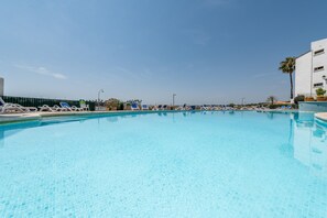 A clear blue pool with lounge chairs and a white building in the background.