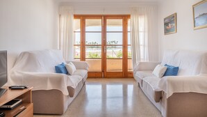 A room with two white sofas, a TV, and a balcony with a view. - Vacation Apartment “Carabela Dali 113” Close to the Beach with Sea View and Pool (Alcudia)
