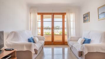 Una habitación con dos sofás blancos, una televisión y un balcón con vistas.