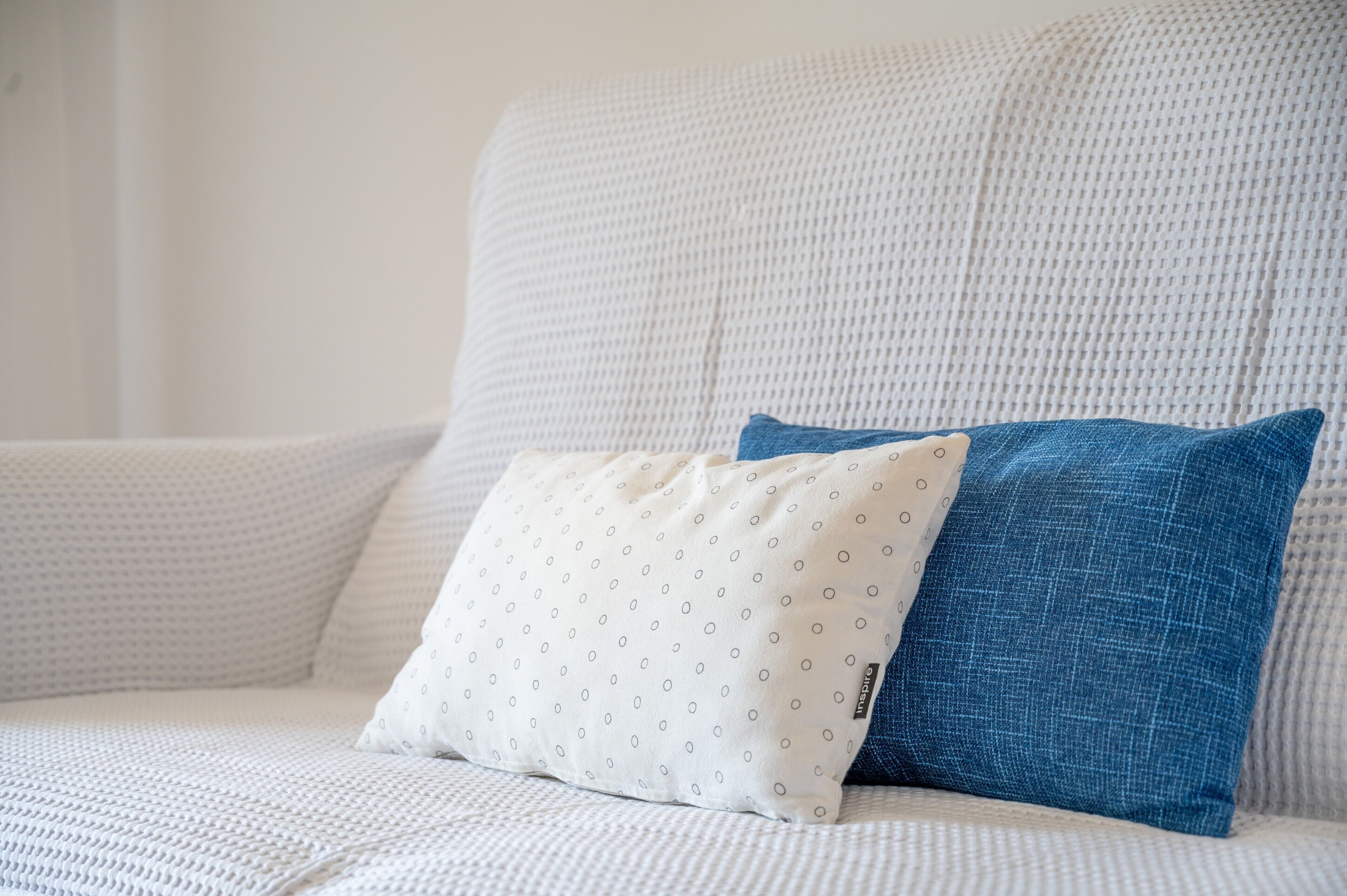 Un sofá blanco con una almohada azul y otra almohada blanca con un diseño.