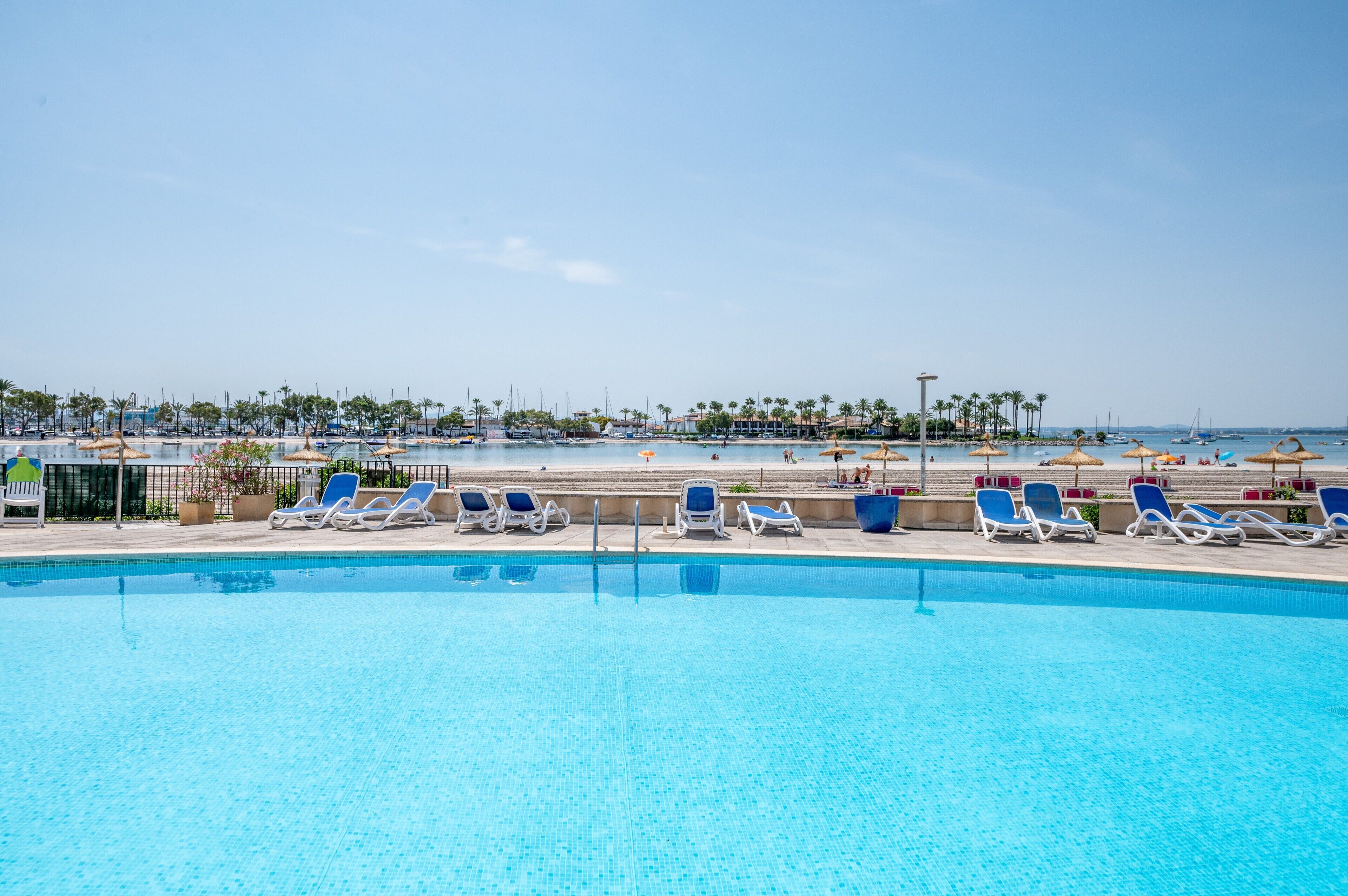 Una piscina con sillones de playa, una playa al fondo y un cielo despejado.