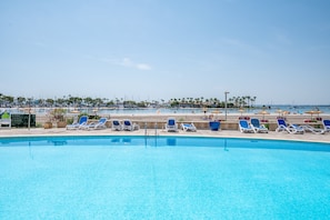 Une piscine avec des chaises longues, une plage en arrière-plan et un ciel dégagé.