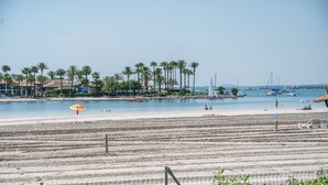 A beach with a fence, palm trees, and boats in the water. - Vacation Apartment “Carabela Dali 113” Close to the Beach with Sea View and Pool (Alcudia)