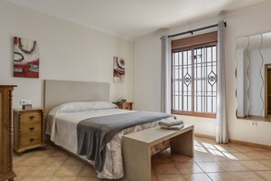 A bedroom with a bed, bedside tables, a bench, a window with bars, and artwork on the walls. - Apartment "Casa Ainhoa" with A/C & Terrace & WIFI (Conil)