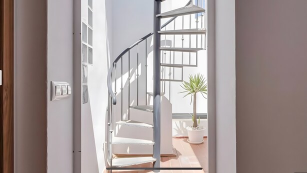 A spiral staircase leading to a balcony with a potted plant.