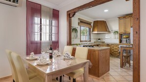 A dining area with a table set for four, a kitchen with wooden cabinets, and a large window with curtains.
