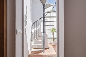 Un escalier en colimaçon avec des rampes en métal et un pot de fleurs placé sur la plateforme.