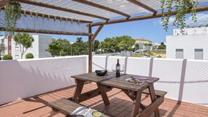 Un tavolo di legno all'aperto con una bottiglia, bicchieri, un menù e un libro su un patio in mattoni sotto una pergola.