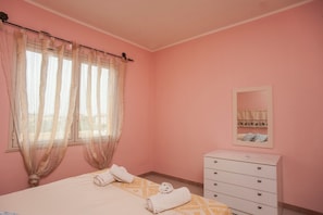 Une chambre aux murs roses, avec un lit, une commode blanche et un miroir accroché au mur.