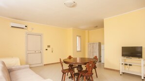 A dining area with a round table and chairs, a sofa, a television on a stand, and a door.