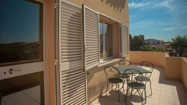 A balcony with a table and chairs, a sliding glass door, and a window with shutters.