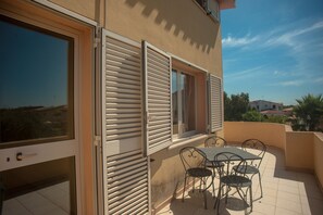 A balcony with a table and chairs, a sliding glass door, and a window with shutters.