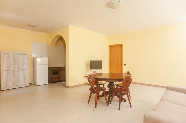 A dining area with a round table and chairs, a kitchen with a refrigerator and stove, and a door.