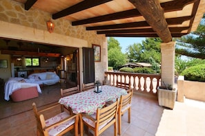 Un espace extérieur abrité, doté d’une table et de chaises, d’un mur en pierre et offrant une vue sur la verdure.