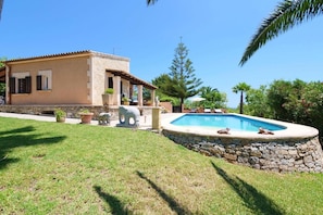 Une maison avec une piscine, des murs en pierre et un jardin avec de la pelouse et des plantes.