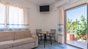 A room with a sofa, a table with chairs, a TV mounted on the wall, and a sliding glass door leading to an outdoor area. - Studio Apartment 'Villa Erica Appartamento Lesley' with Mountain View, Wi-Fi and Air Conditioning (villa san pietro)