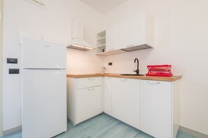 A compact kitchen with white cabinets, a built-in oven, a sink, and a red basket on the countertop.