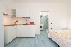 A compact room with a kitchenette, a washing machine, and a bed with a patterned bedspread.