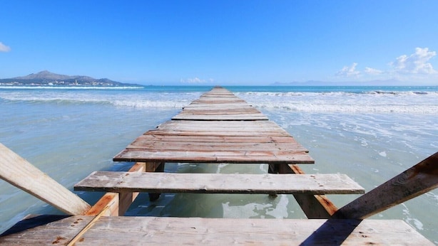 Un muelle de madera que se adentra en un mar tranquilo con cielos despejados.