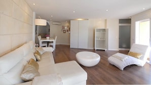 Una sala de estar moderna con sofá, otomanas y sillones, un comedor con mesa y sillas, y un vestidor.