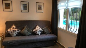 Un sofá de color oscuro con cojines de estampado de cebra, una mesita y una ventana con vista a una piscina.