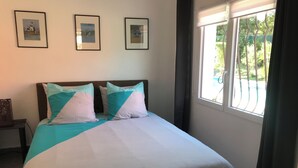 Una cama con ropa de cama blanca y aguamarina, una mesita de noche y tres cuadros en la pared.