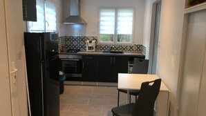 Cocina compacta con estufa, horno y pileta. Hay una mesa de comedor con una silla y una ventana con persianas.