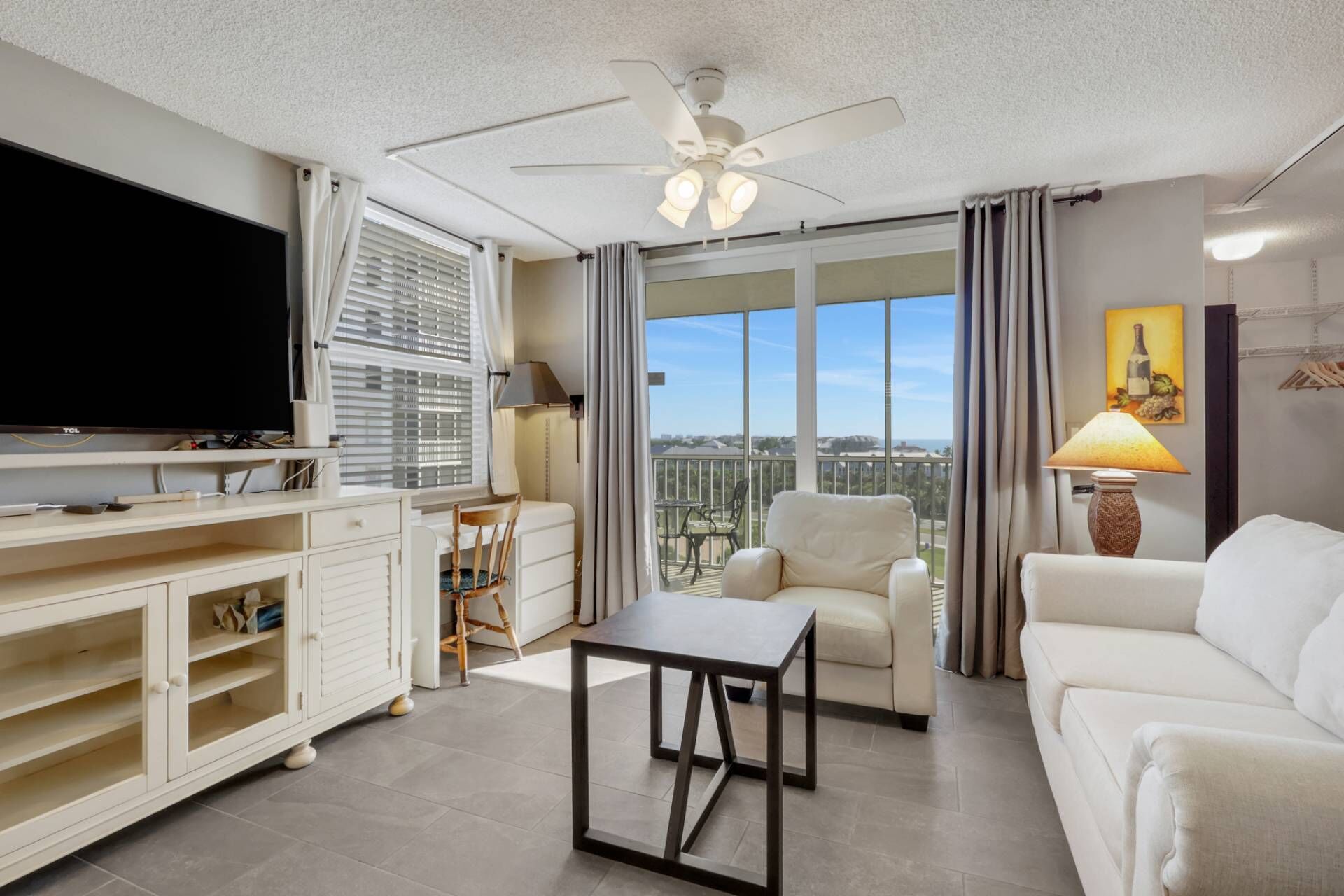 A modern living room with a flat-screen TV, a ceiling fan, a dining table, a sofa, and a balcony with a view.