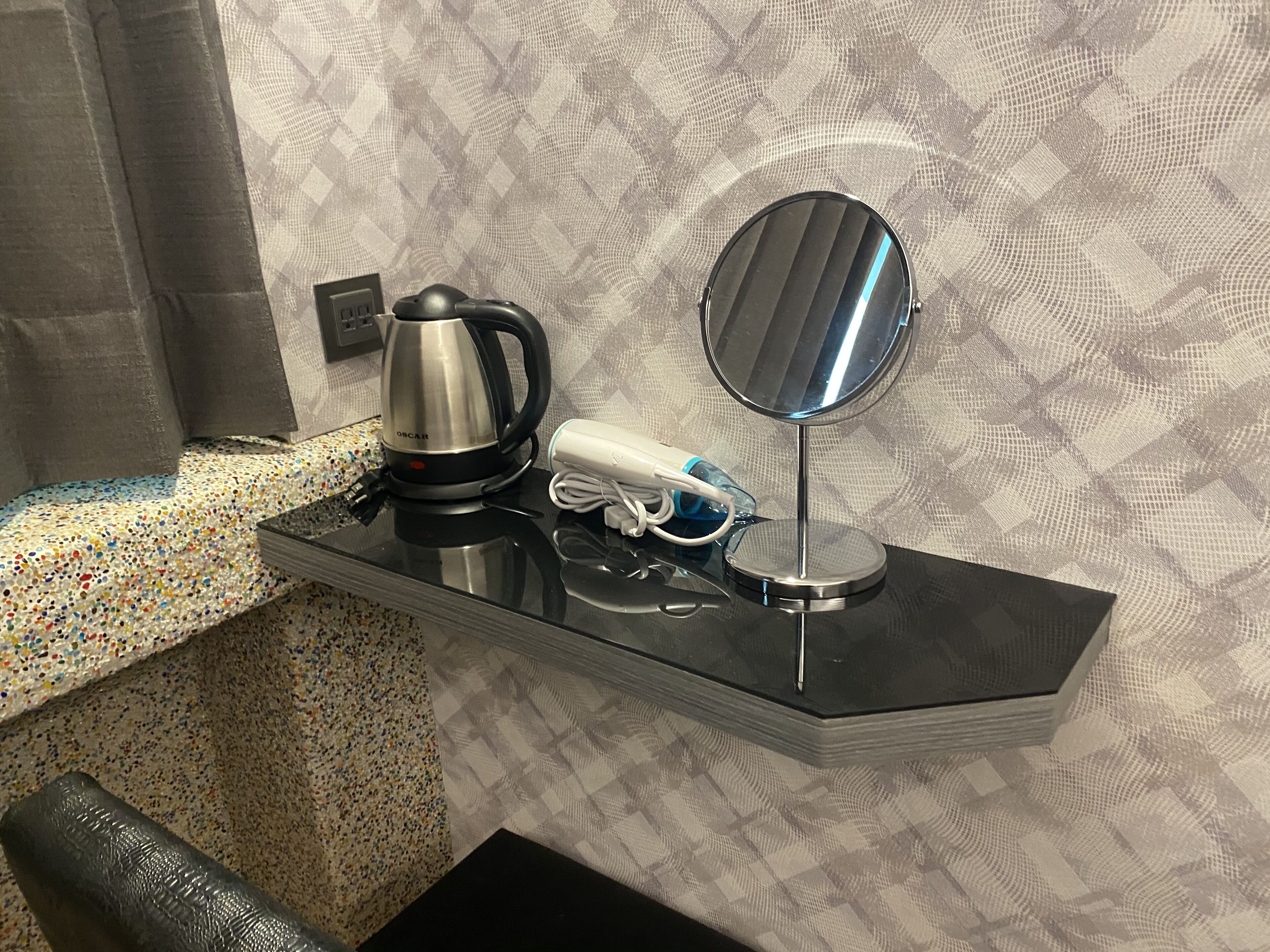 Un tocador de baño con cafetera, secador de pelo y espejo.