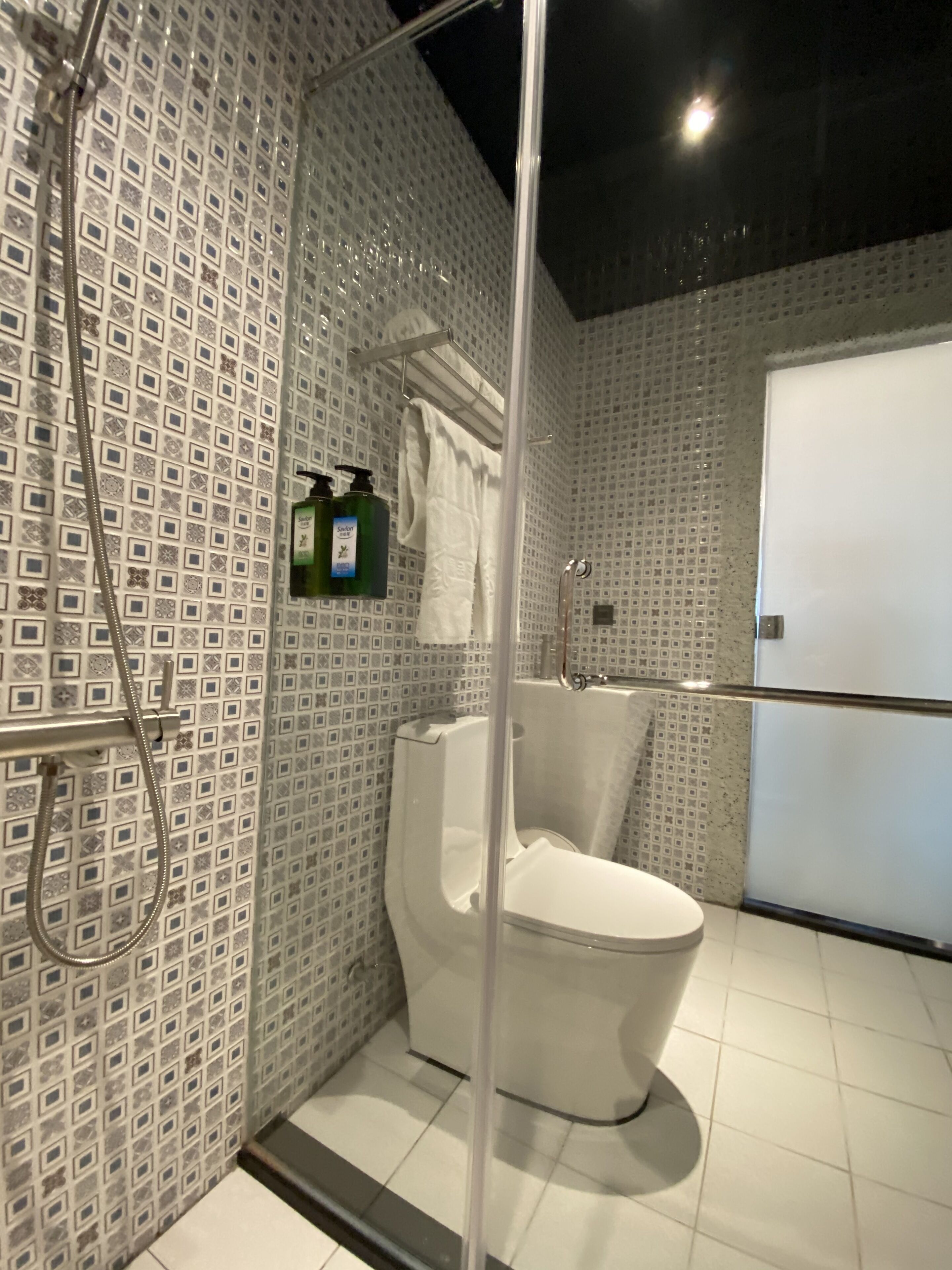 A modern bathroom with a glass-enclosed shower, a white toilet, and patterned tile walls.
