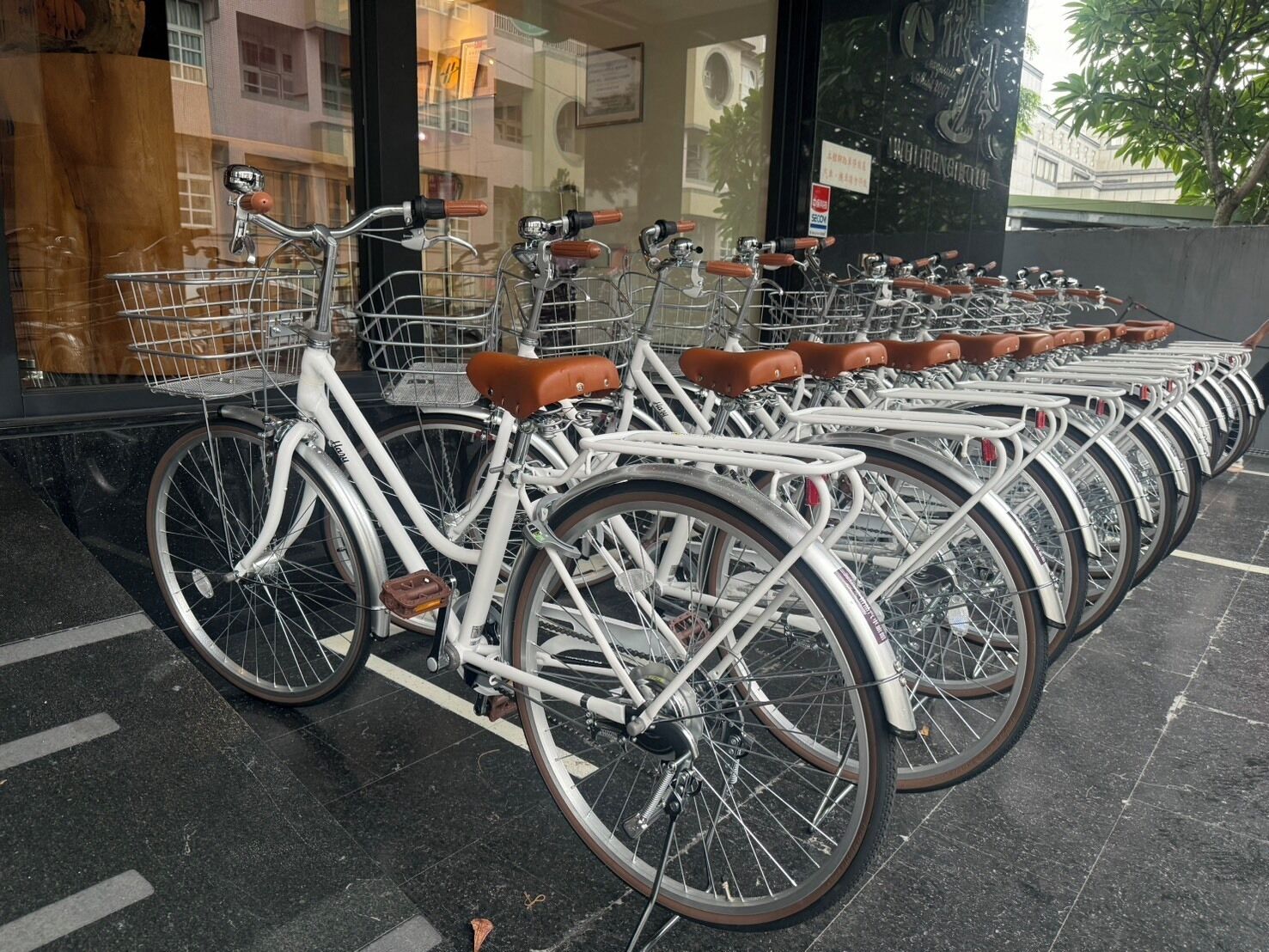 A row of white bicycles with brown leather seats parked outside a building.