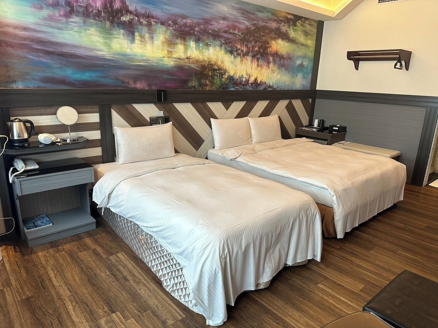 A hotel room with two beds, a painting on the wall, a desk with a phone, and a nightstand.
