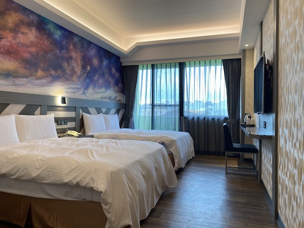 A hotel room with two beds, a desk, a chair, a TV, and a large window with curtains.