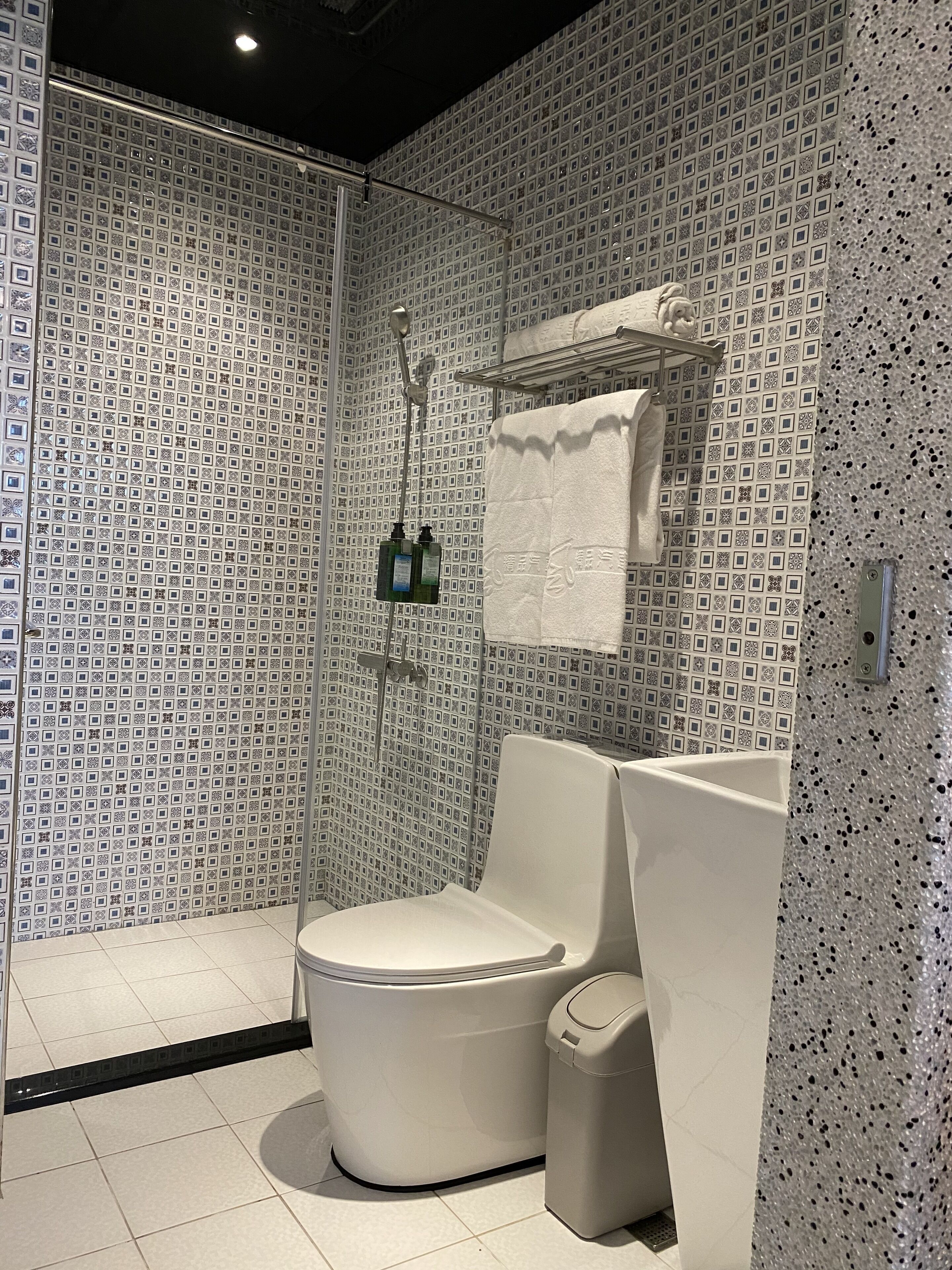 A modern bathroom with a patterned wall, a toilet, a shower, and a towel rack.