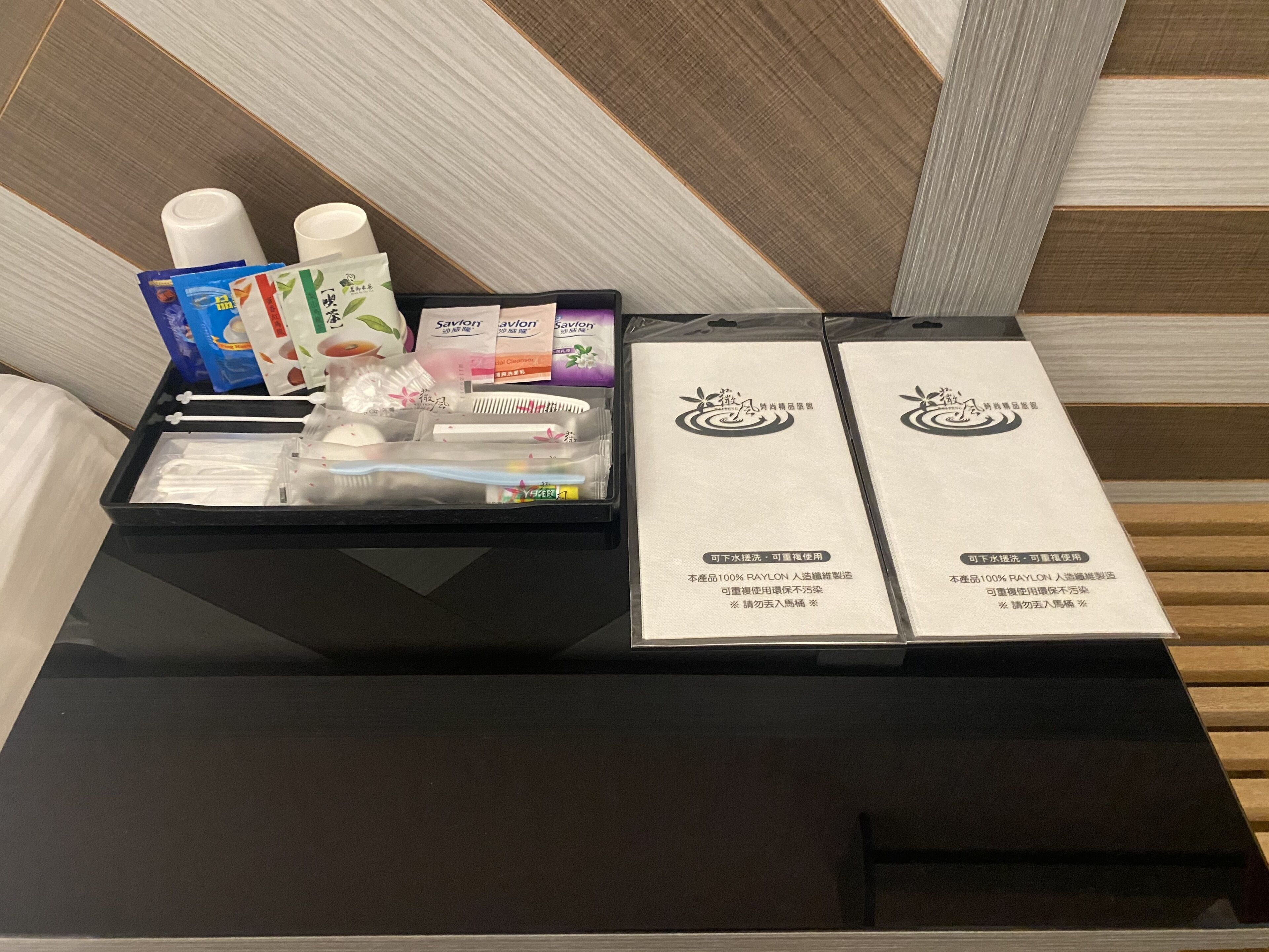 A hotel room with a black tray table holding toiletries and a pair of slippers.