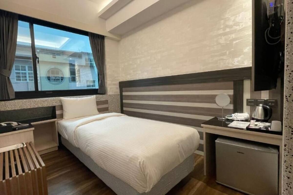 Ein modernes Hotelzimmer mit Bett, Nachttisch und einer kleinen Küchenzeile.