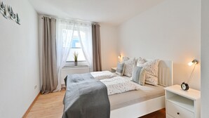 Et soveværelse med en seng, et natbord, en lampe og et vindue med gardiner.