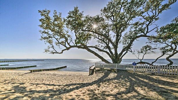 En strand med et stort træ, et hvidt hegn og en træbro.