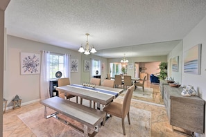 A dining area with a long table, chairs, and a chandelier. There are framed artworks on the walls and a large mirror reflecting the room. - Naples Condo w/ Enclosed Balcony & Lake Views! (Naples)