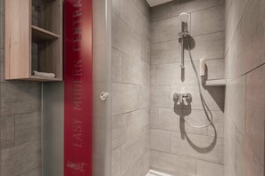 Una ducha moderna con azulejos grises, un cabezal de ducha de mano y un panel de control montado en la pared.